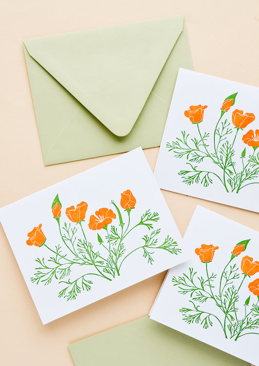 A set of white greeting cards with orange poppy flowers printed on front, paired with pastel green envelopes.