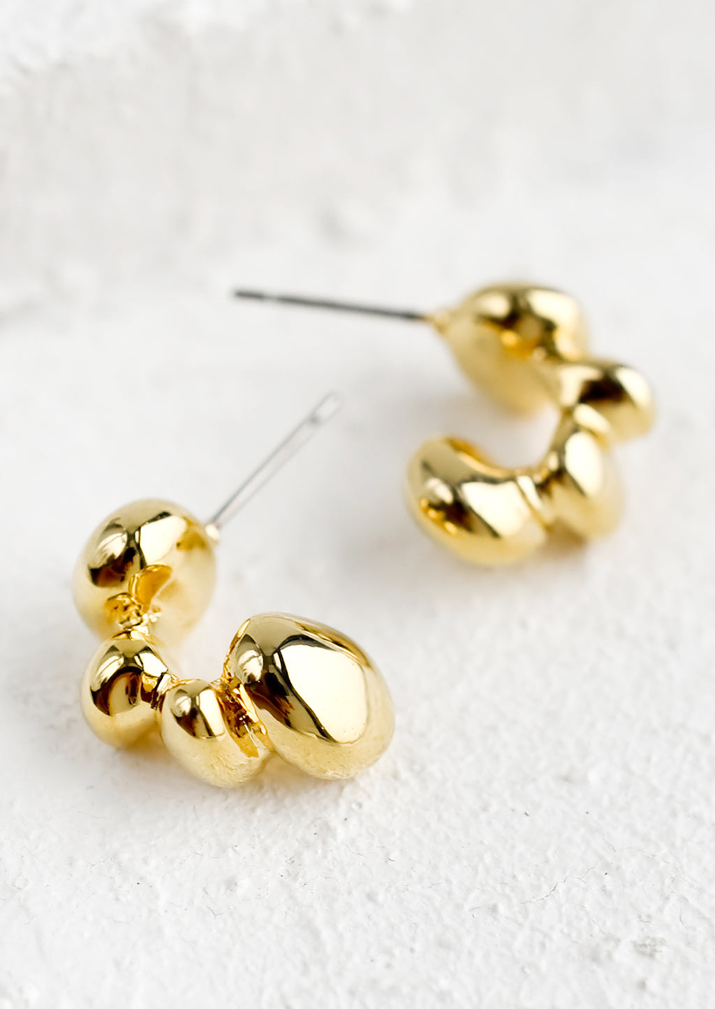 2: A pair of gold hoop earrings in melty blob shape.