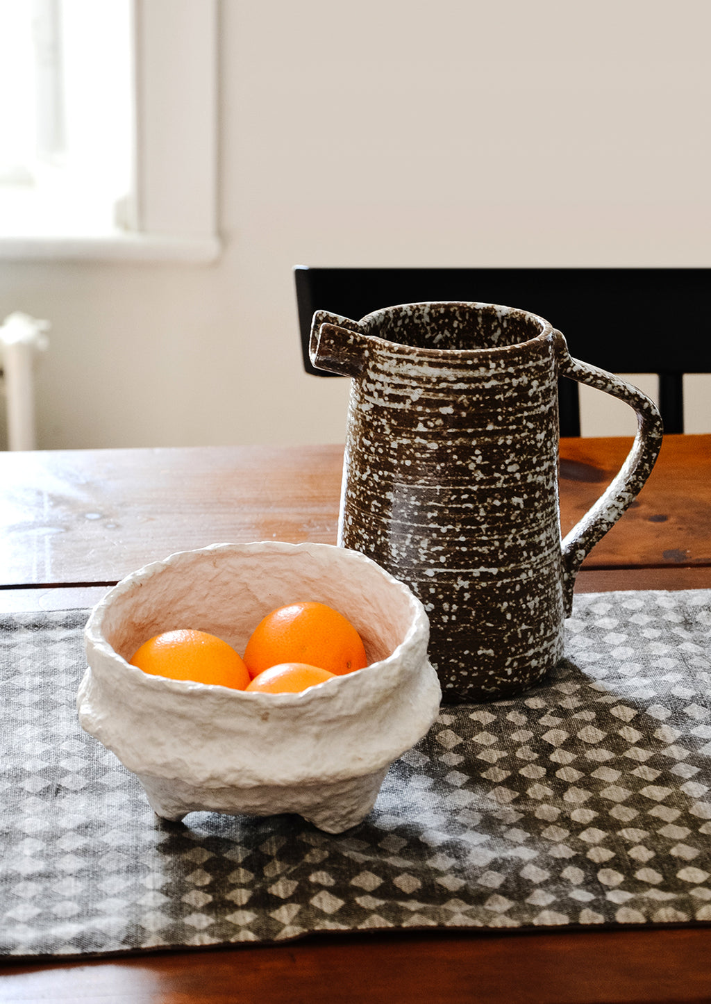 White: Tabletop scene with ceramic pitcher and white paper mache bowl with tangerines