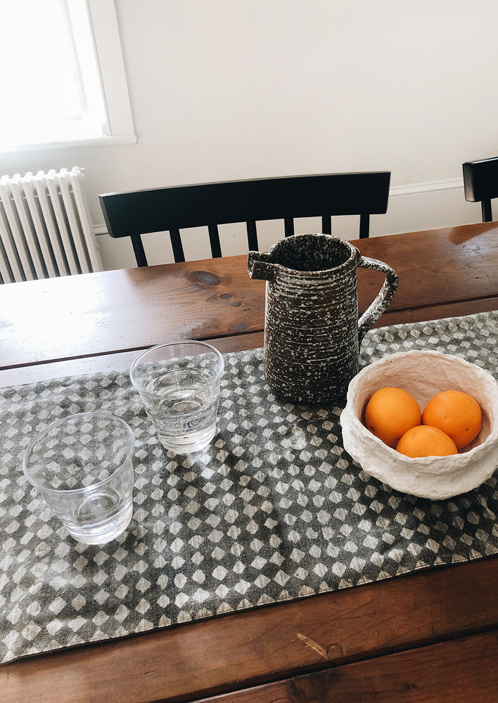 Dining table with table runner, water glasses, pitcher and bowl of oranges