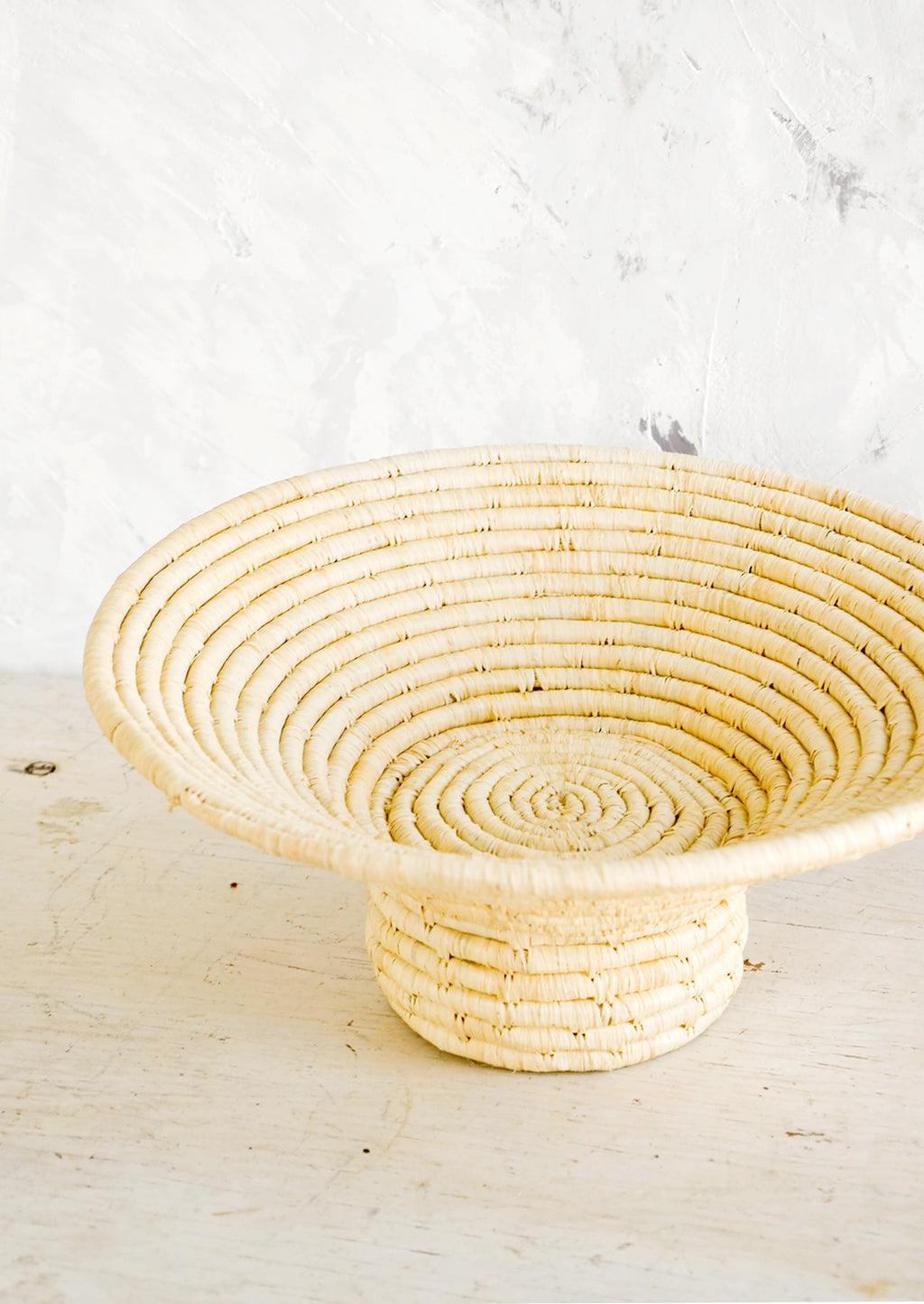 1: Footed pedestal bowl made from natural woven raffia, sitting on a table