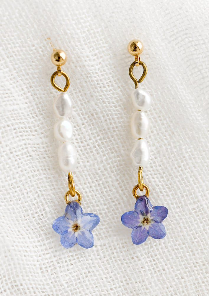 A pair of pearl drop earrings with dried floral charms at bottom.