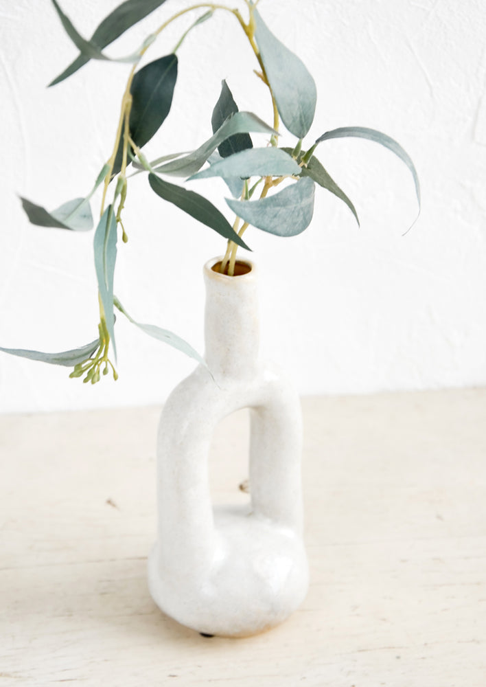 2: An off-white ceramic vase with eucalyptus leaves.