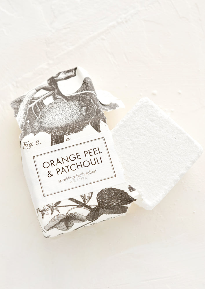 Orange Peel & Patchouli: White bath fizz cube emerging from black and white botanical packaging.