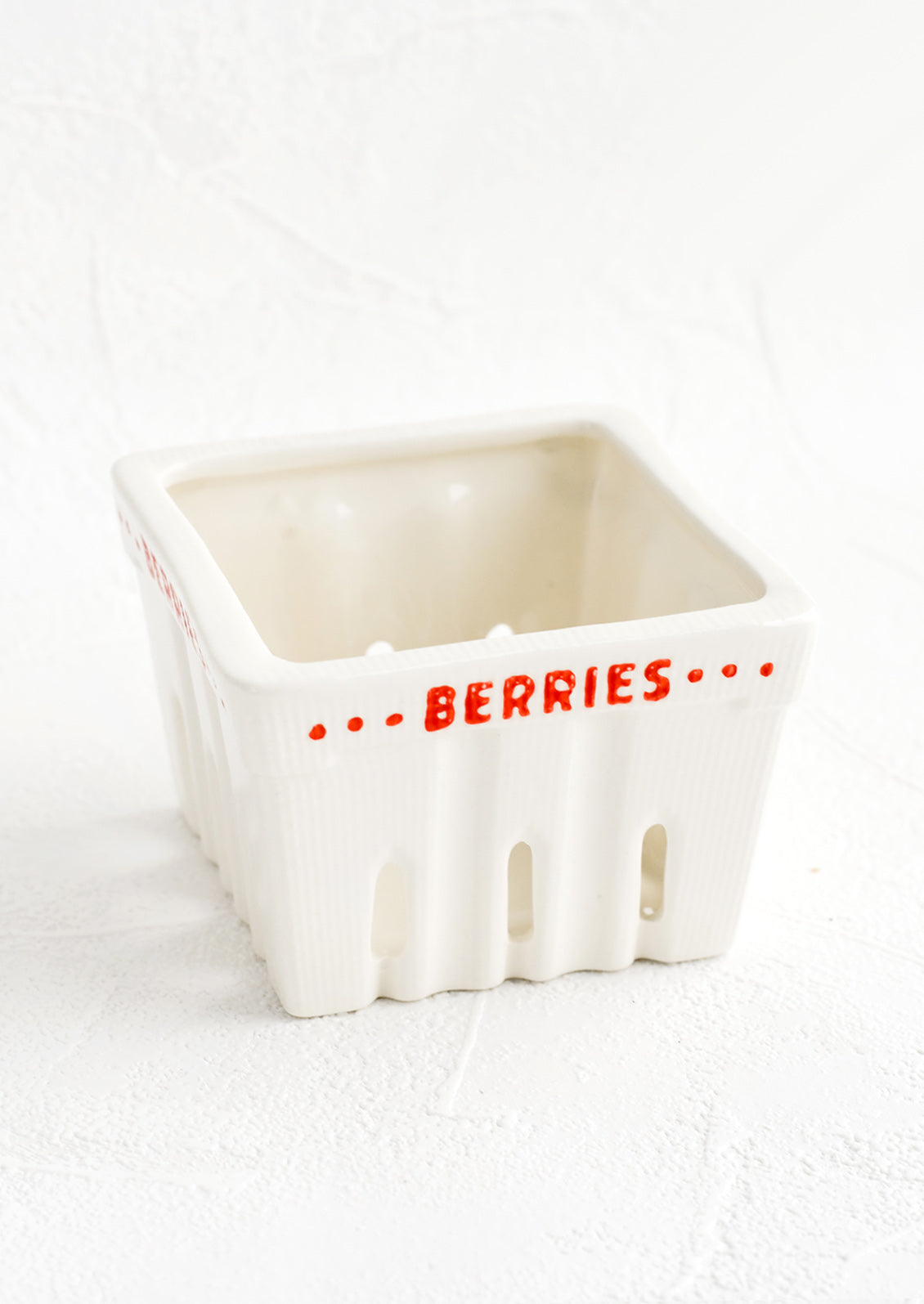 A white ceramic basket designed to look like a berry basket with "Berries" printed in red lettering.