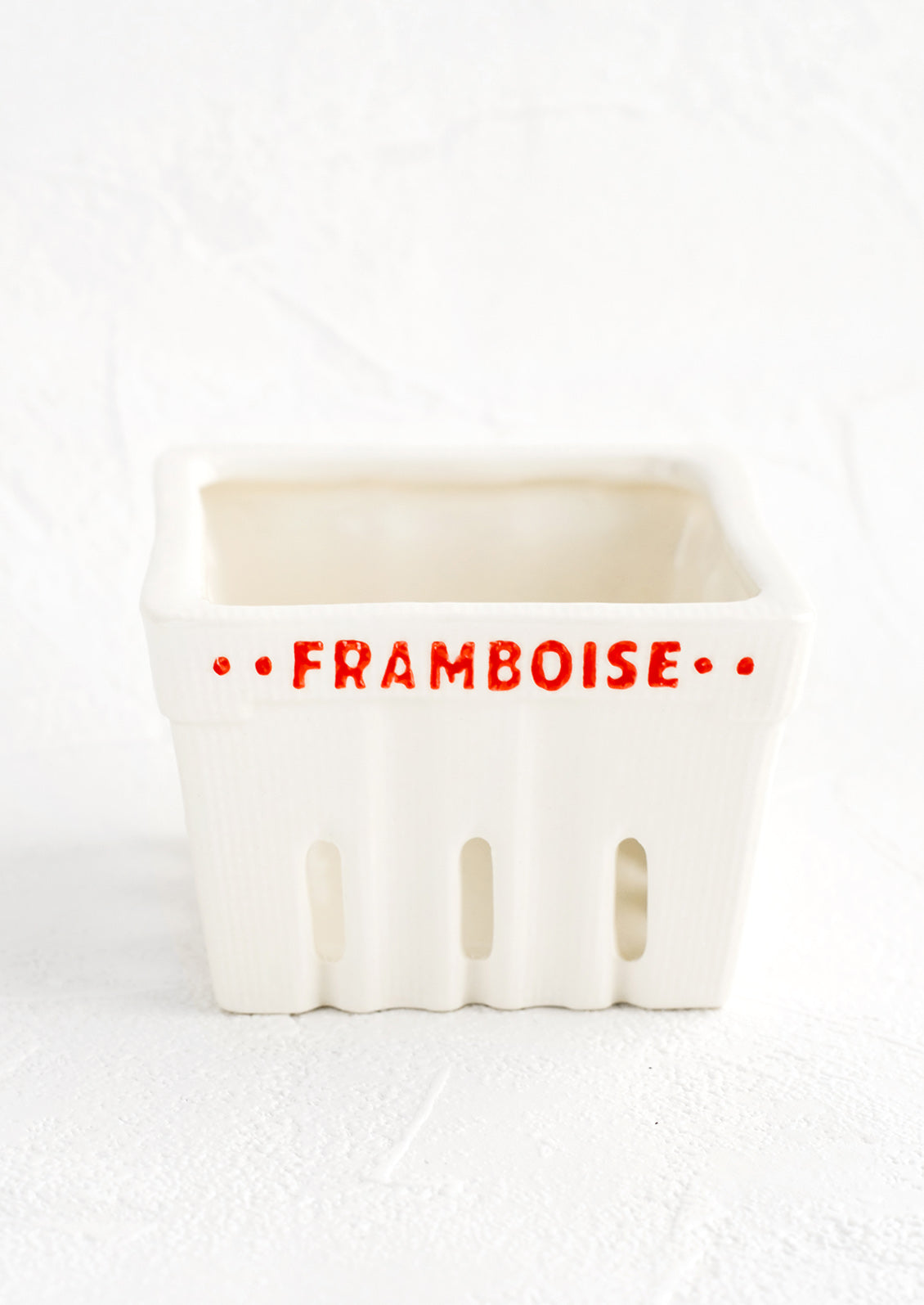 A white ceramic basket designed to look like a berry basket with "Framboise" printed in red lettering.