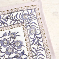 1: Tablecloth folded on a table. Features a bordered floral pattern in grey/lavender.
