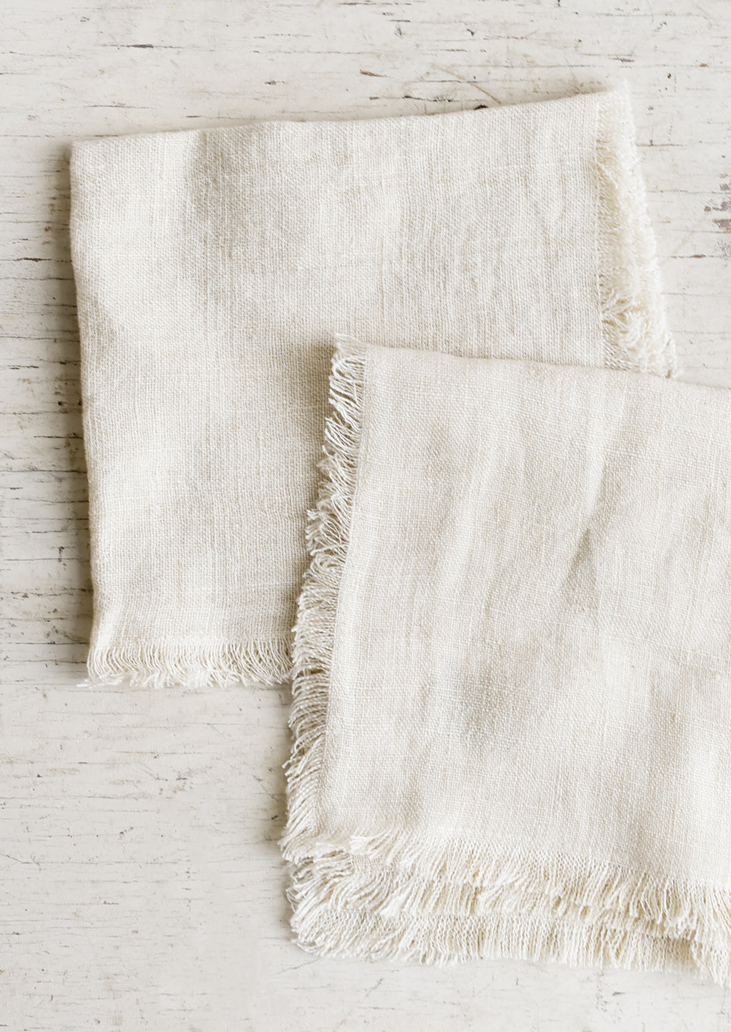 Cream: Folded cream colored linen napkins with frayed edges.