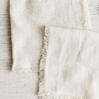 Cream: Folded cream colored linen napkins with frayed edges.