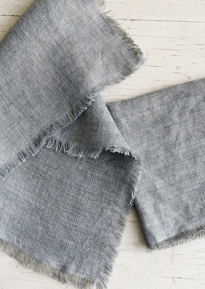 Folded grey colored linen napkins with frayed edges.