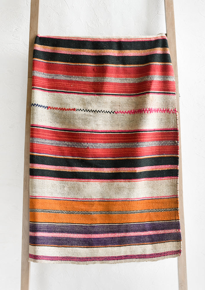A vintage frazada textile in varied stripe pattern in red, tan, orange and purple.