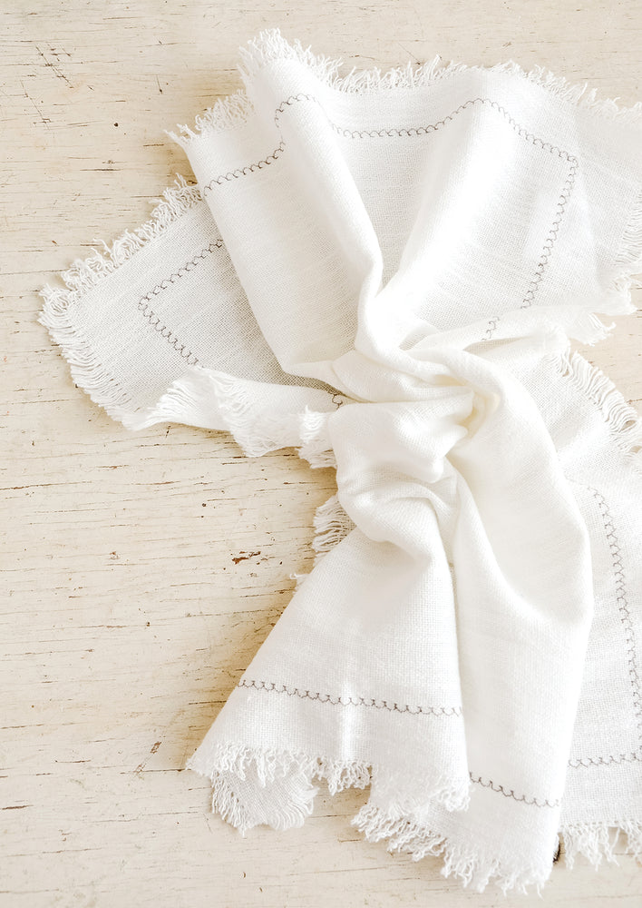 White cotton dinner napkin with frayed edges and stitched border detail