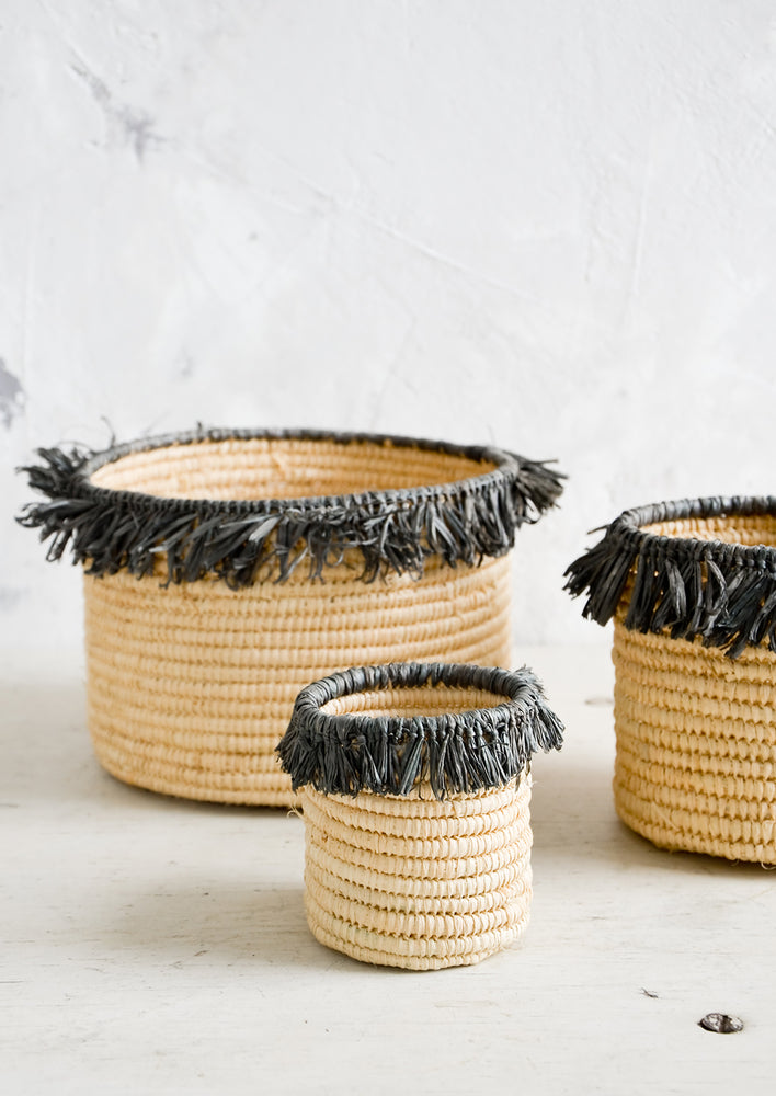 Round, natural raffia baskets with dark grey fringed raffia trim around top