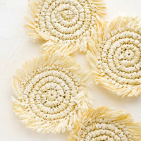 Ivory: Four round straw coasters with fringed trim in natural ivory.