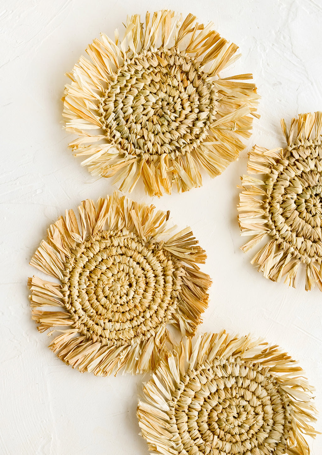 Tan: Four round straw coasters with fringed trim in natural tan.