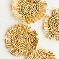 Tan: Four round straw coasters with fringed trim in natural tan.