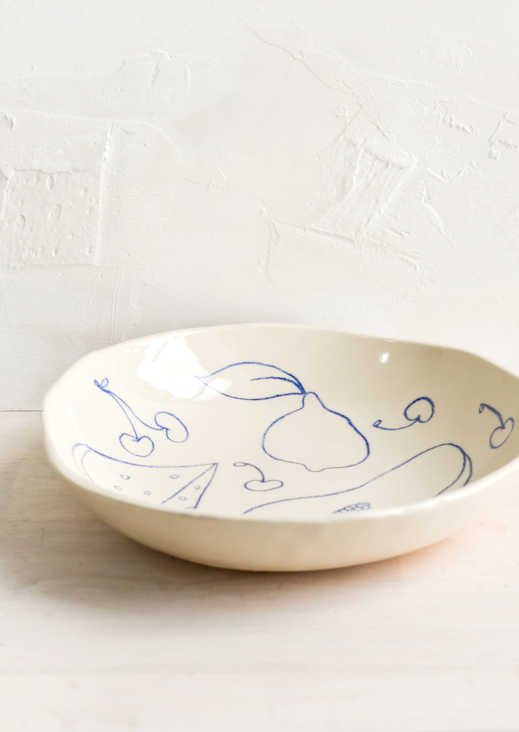 2: A round serving bowl in natural ceramic with blue fruit line drawings.
