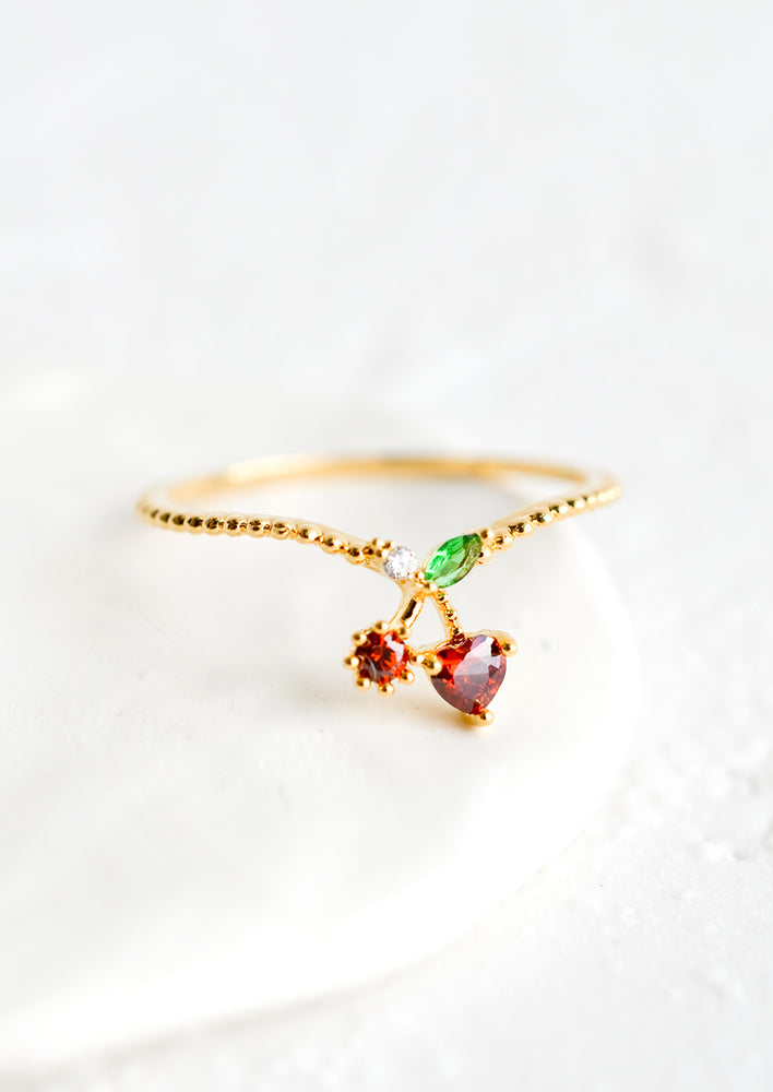 A gold ring with beaded texture and cherry shaped crystal front.