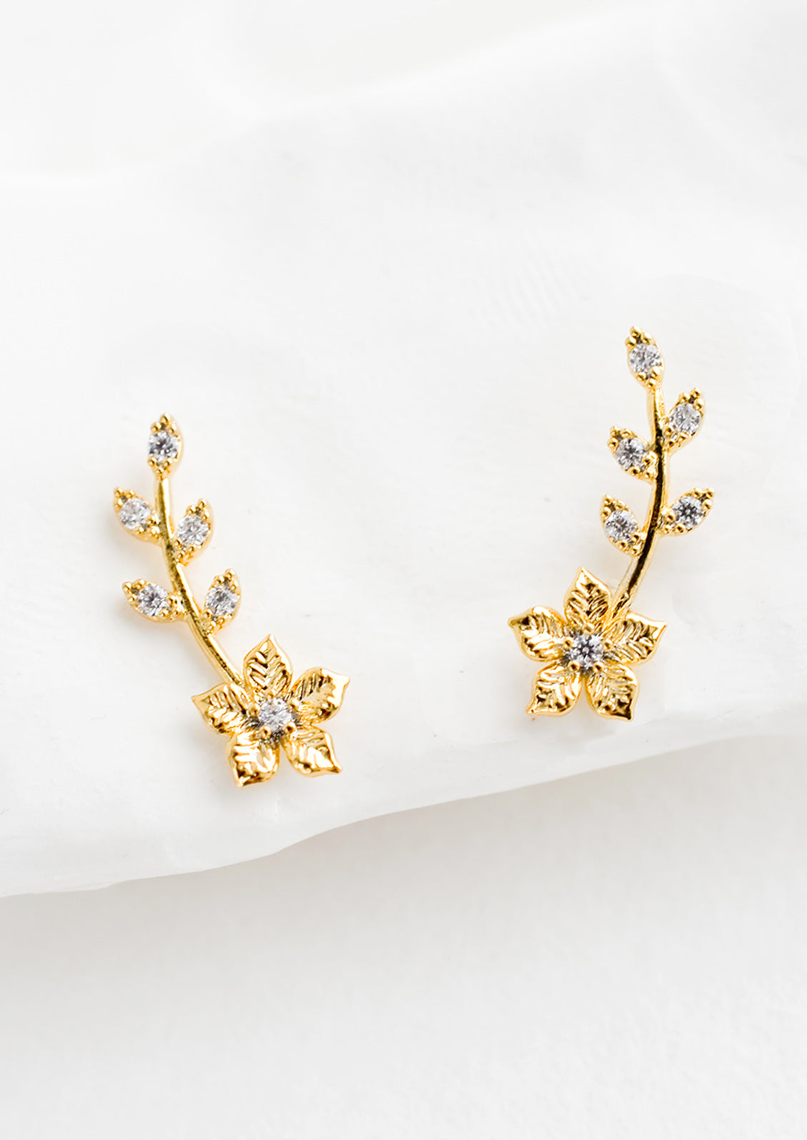 A pair of gold climber stud earrings with floral design decorated with crystals.