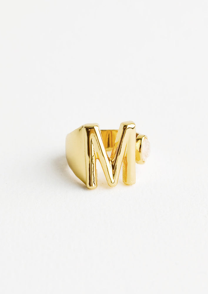Yellow gold ring with letter M and oval glass crystal, and wide adjustable band.