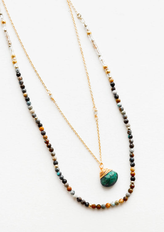 A two-layer gold necklace with one strand of small, round multi-color stones and another of the thin gold chain and green gemstone pendant.