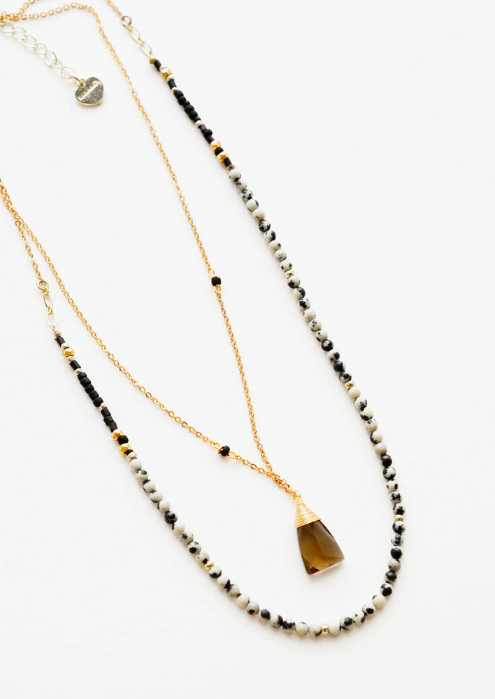Dalmatian Jasper: A two-layer gold necklace with one strand of small, round cream and black stones and another of the thin gold chain and brown gemstone pendant.