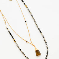 Dalmatian Jasper: A two-layer gold necklace with one strand of small, round cream and black stones and another of the thin gold chain and brown gemstone pendant.
