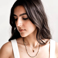 2: Model wears layered necklace and white tank top.