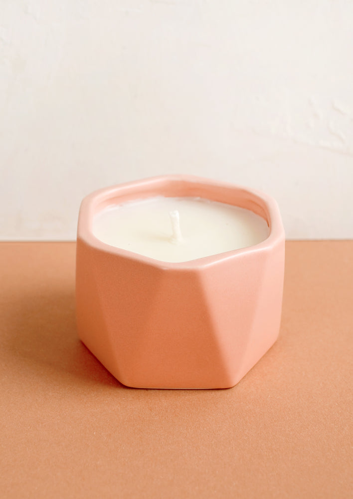 A small candle in peach faceted ceramic vessel.