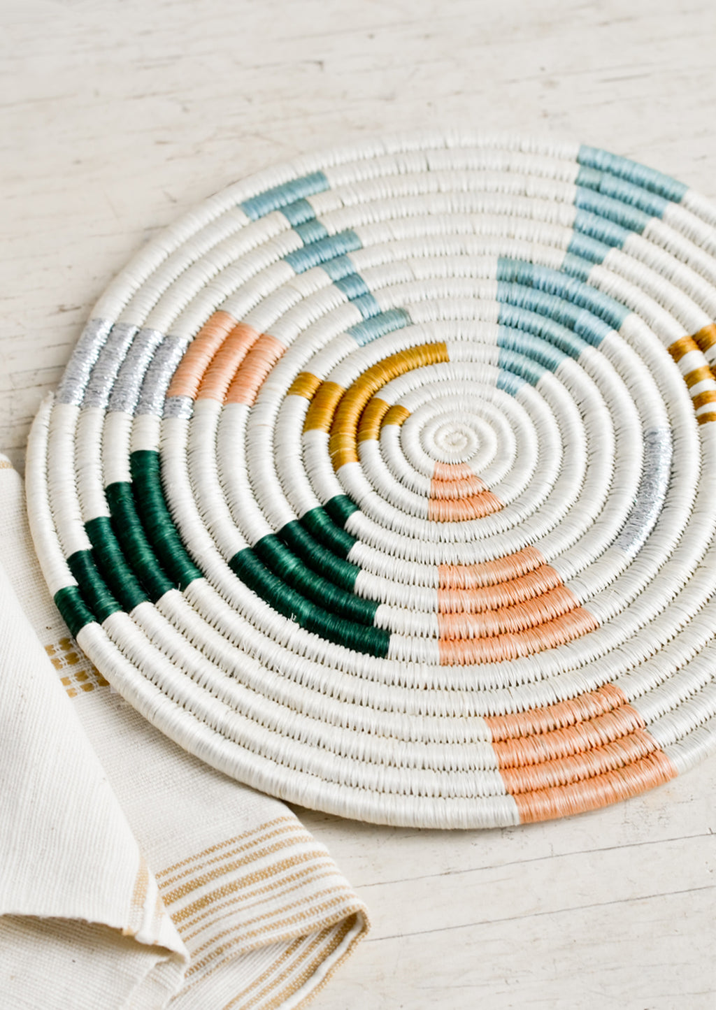 3: A round trivet in white with metallic and pastel design.