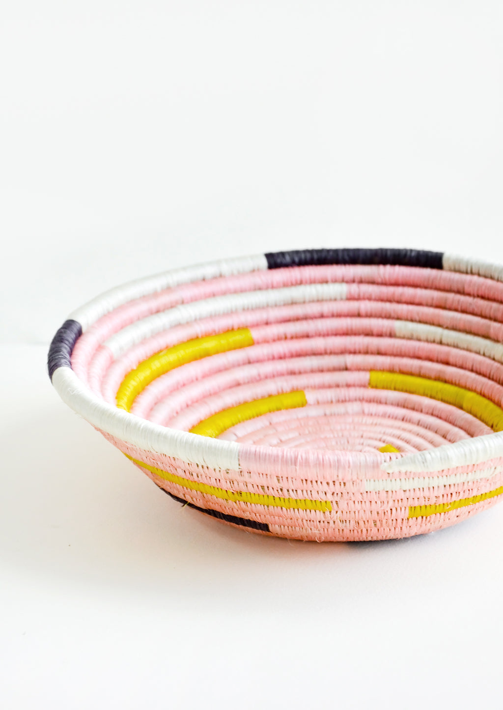 2: Round, shallow bowl made from woven sweetgrass in pink, white, yellow and black.
