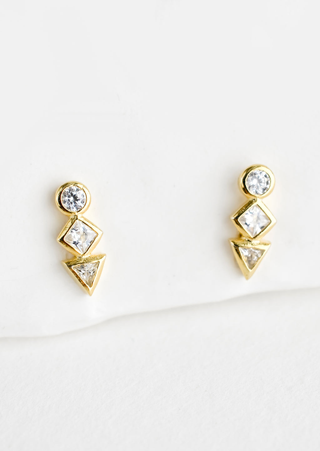 1: A pair of gold stud earrings with a circle, diamond and triangle crystal stacked in a row.