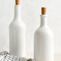 1: Matte white ceramic bottles in short and tall heights, with cork stoppers.