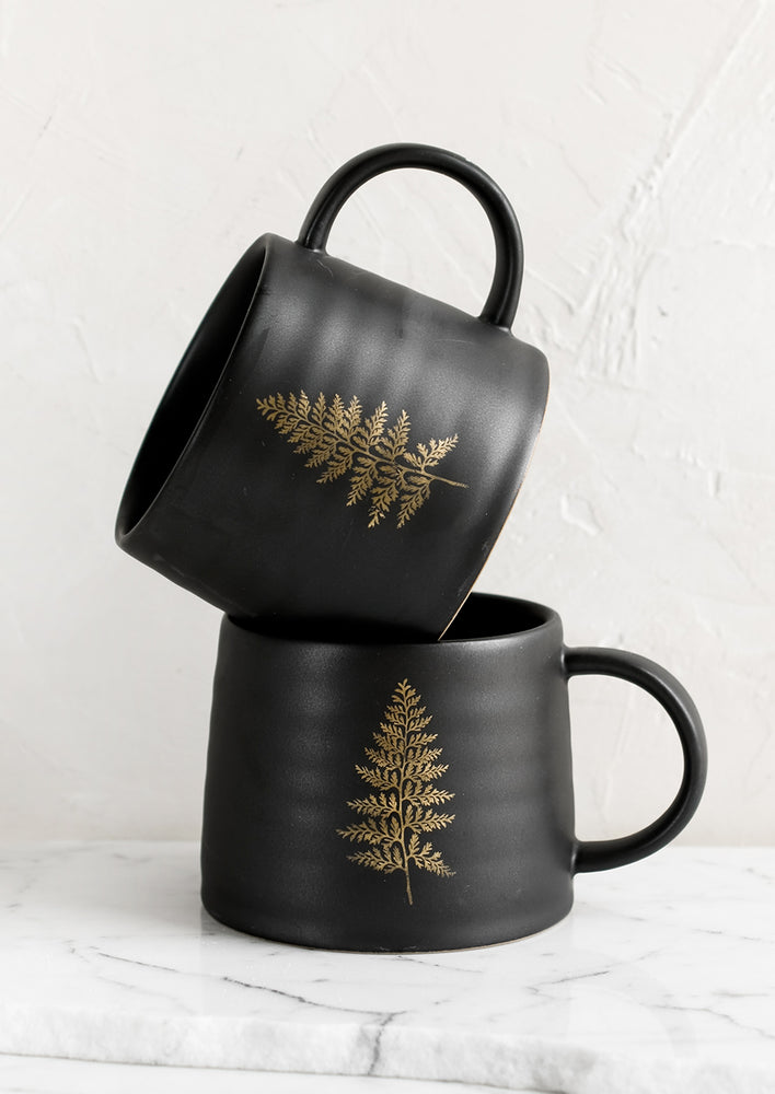 A black ceramic mug with single gold fern print.
