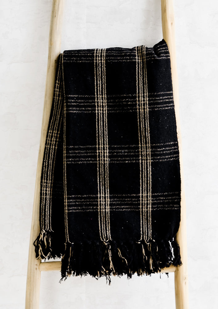 A black cotton throw with beige plaid pattern and fringe trim.