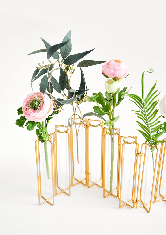Multi-stem vase composed of nine glass vials side by side, resting inside individual compartments on a brass metal frame.