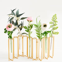 2: Multi-stem vase composed of nine glass vials side by side, resting inside individual compartments on a brass metal frame.