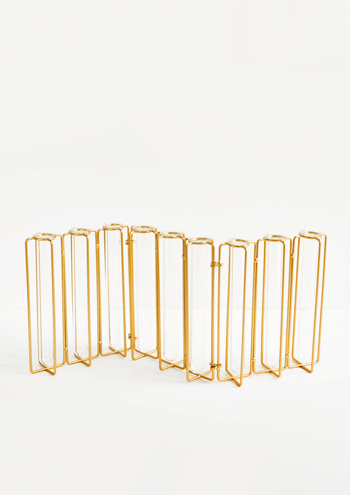 4: Multi-stem vase composed of nine glass vials side by side, resting inside individual compartments on a brass metal frame.