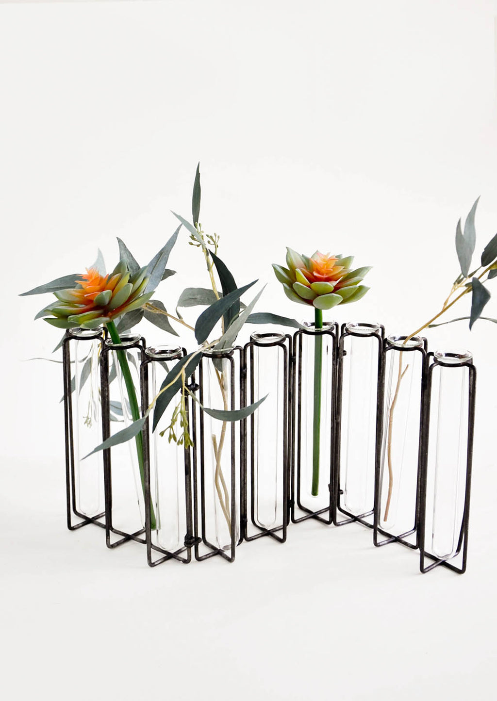 Iron: Multi-stem vase composed of nine glass vials side by side, resting inside individual compartments on a metal frame.