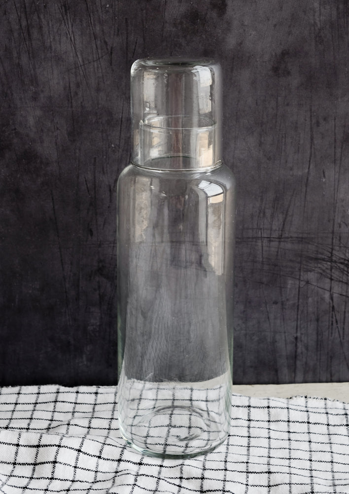 A tall glass decanter with small matching cup that doubles as a lid.