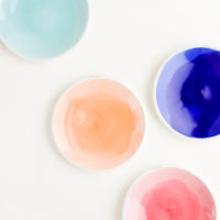 Medium: Four shallow porcelain dishes in light blue, dark blue, pale orange, and pink with shiny finishes and matte white rims.