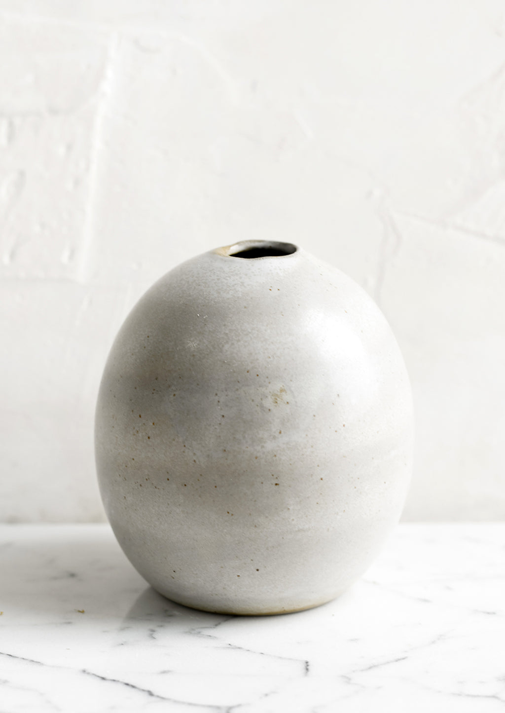 2: A round bud vase in grey ceramic with soft speckles.
