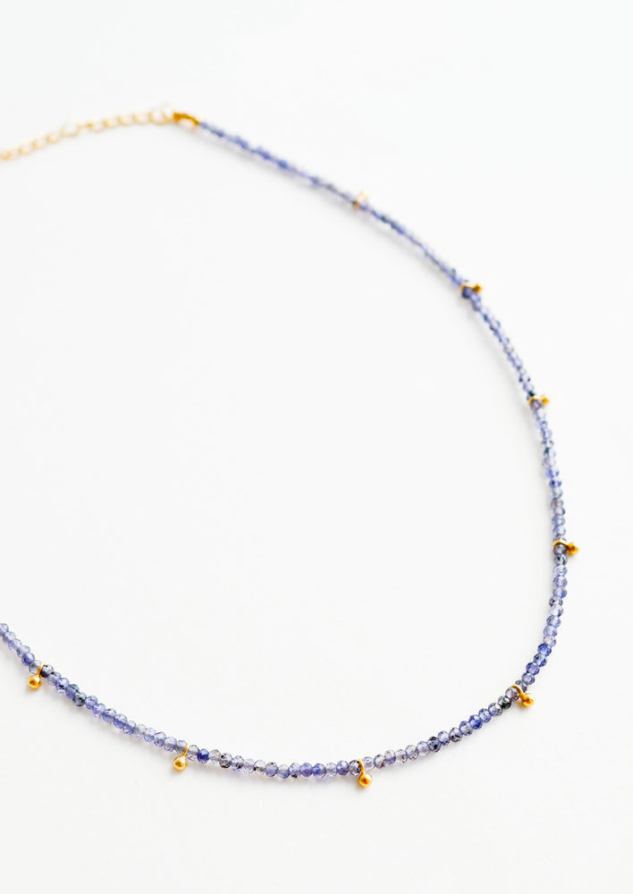A necklace of deep blue stones with evenly spaced gold beads and a golden chain clasp.