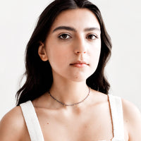 3: Model wears dark blue choker necklace and white tank top.