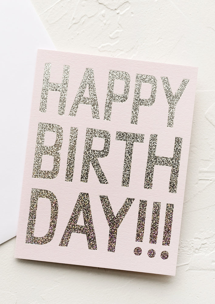 1: A pale pink birthday card with silver holographic glitter text reading "Happy birthday!!!"
