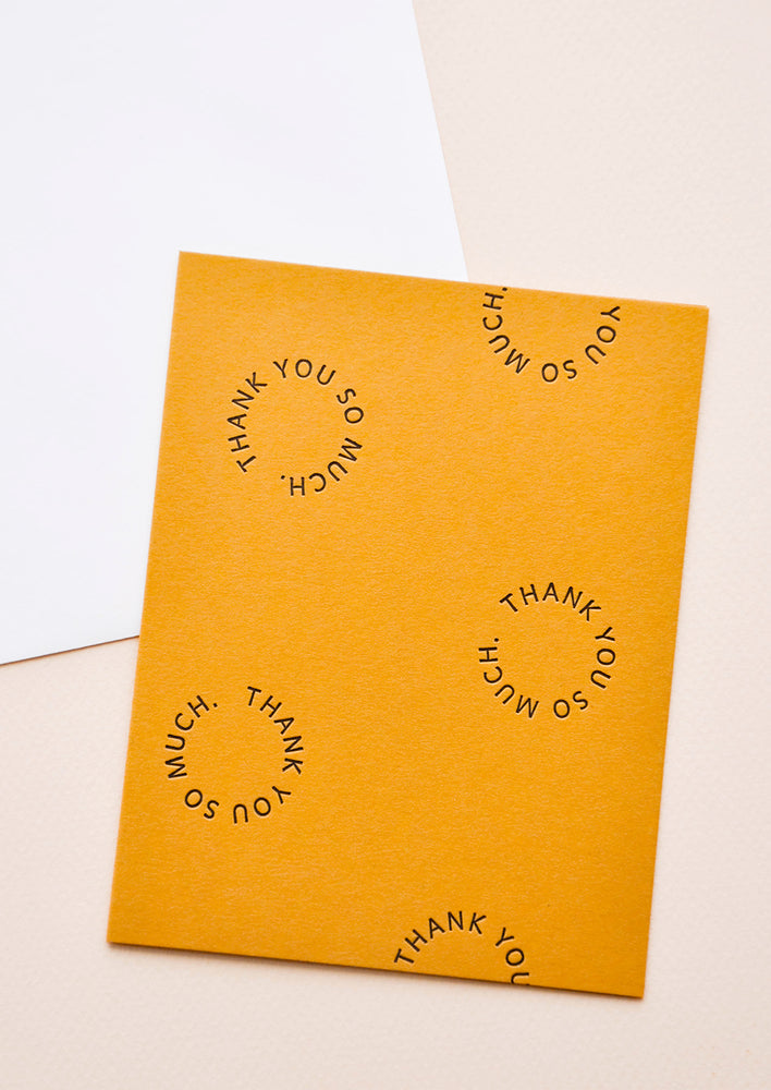 1: Marigold notecard with the text "Thank you so much" set in a circle several times, with white envelope.