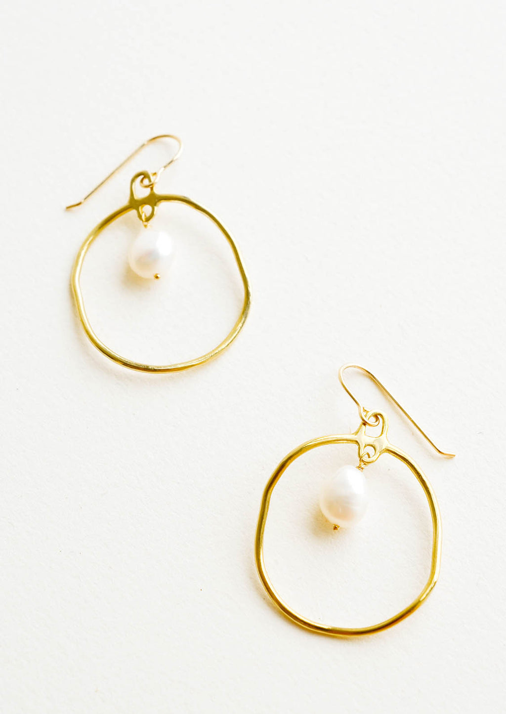 Brass: Circular drop earrings in gold with a small pearl dangling within.