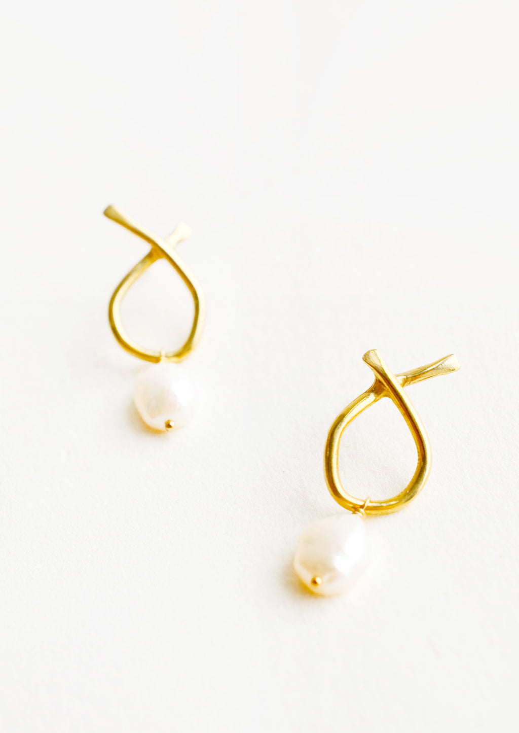 Brass: Pair of brass earrings featuring a slim asymmetrical frame on a post back and dangling pearl.