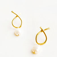 Brass: Pair of brass earrings featuring a slim asymmetrical frame on a post back and dangling pearl.