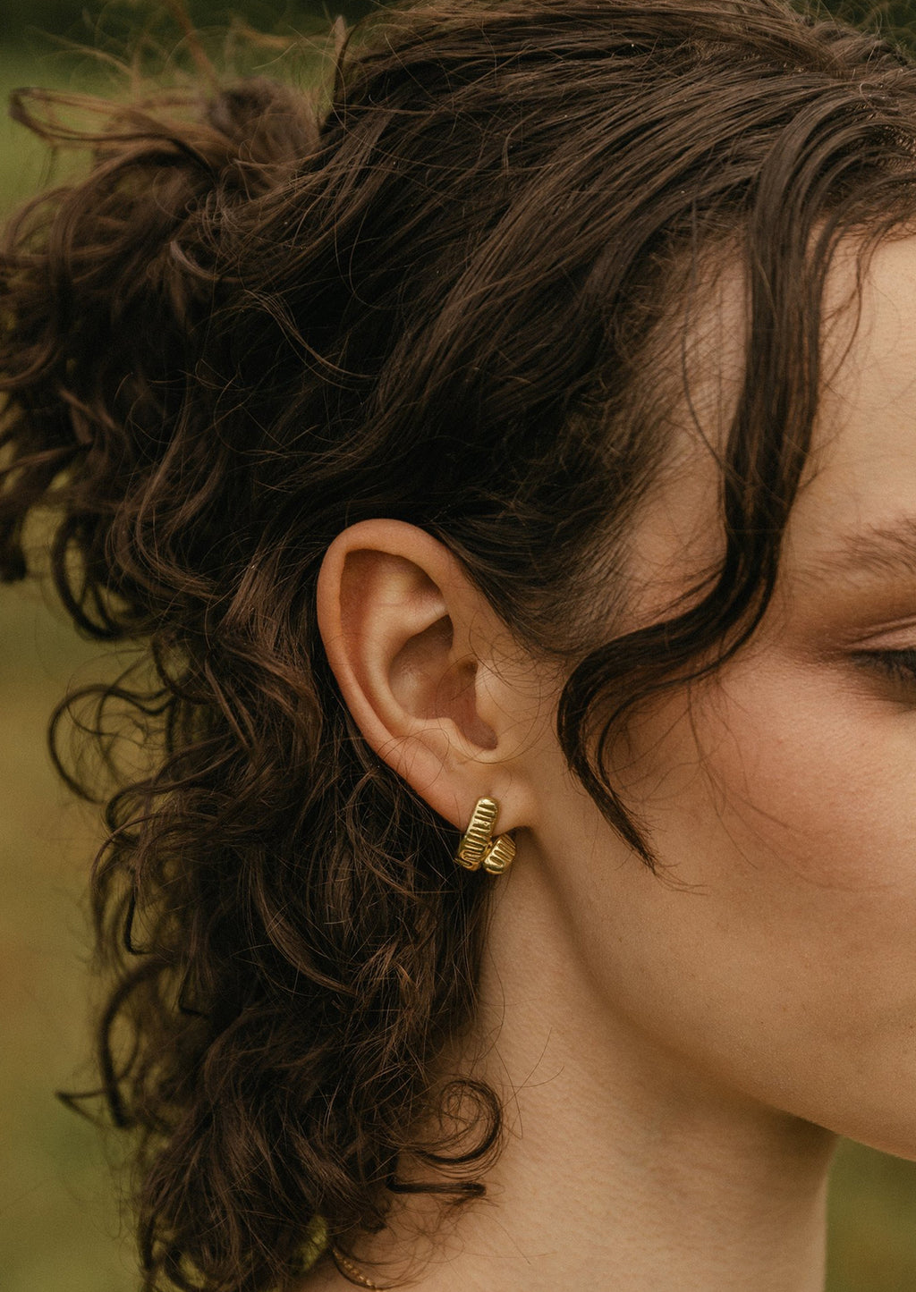 2: A woman wearing a pair of brass earrings.